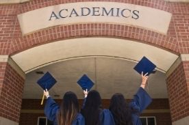 three girls facing backward holding graduation caps in the air.