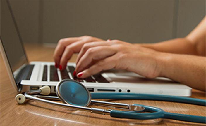 Person typing on laptop with stethoscope.
