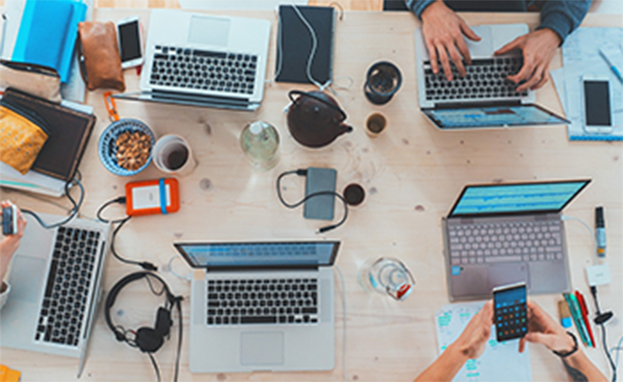 Group of people sitting at table with laptops.