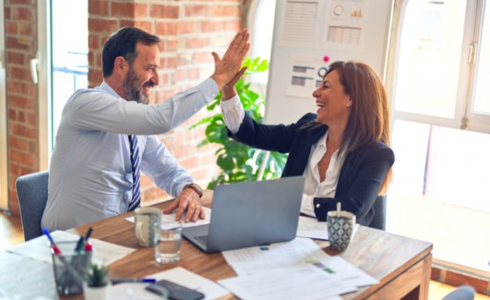 Boss high-fiving employee at work station.
