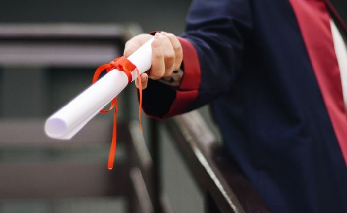 person holding rolled diploma tied with red ribbon.