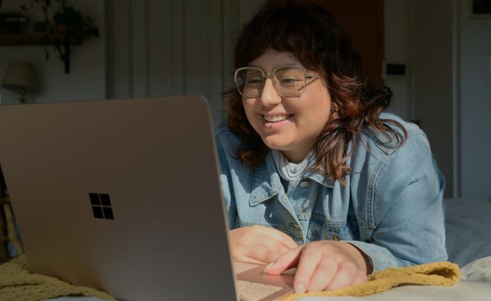 woman in denim shirt wearing glasses using a silver laptop computer.