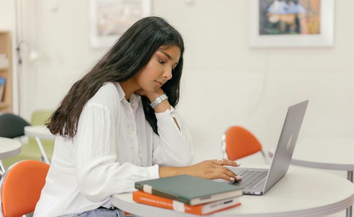 Teen girl using silver laptop in classroom.