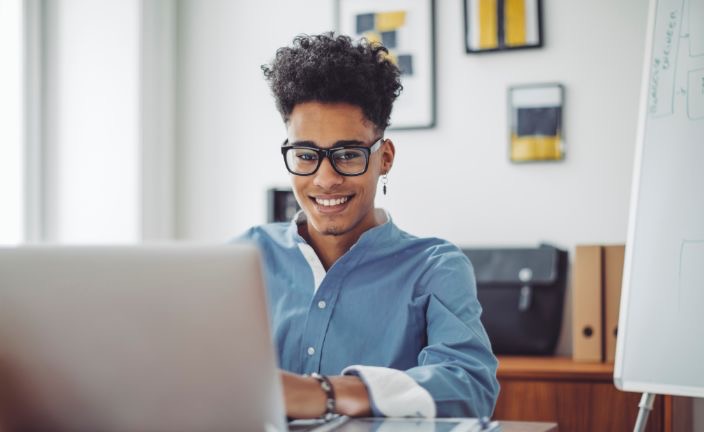 Person with glasses sitting at a table typing on a laptop.