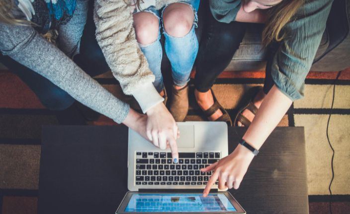 three people pointing at a laptop screen.