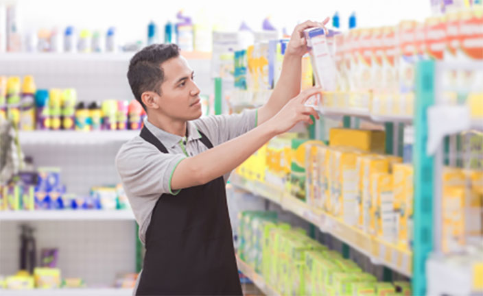 Man with green apron stocking shelves at a supermarket.