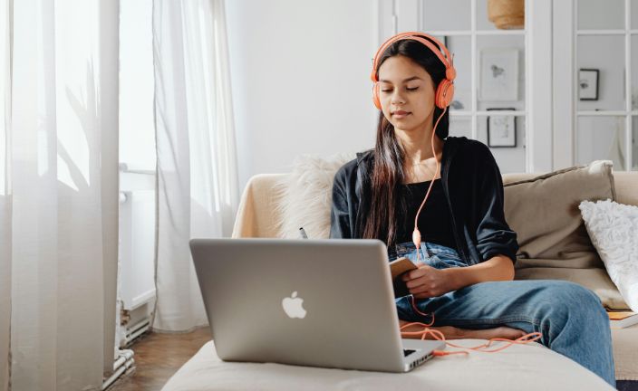 Teen girl wearing headphones using silver Apple laptop.