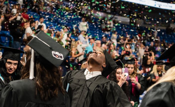 Graduates at commencement ceremony looking up at confetti.