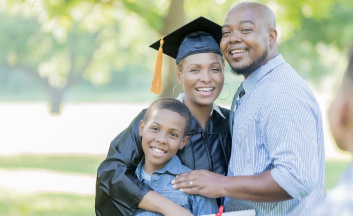 Woman in graduation cap and gown smiling with husband and son.