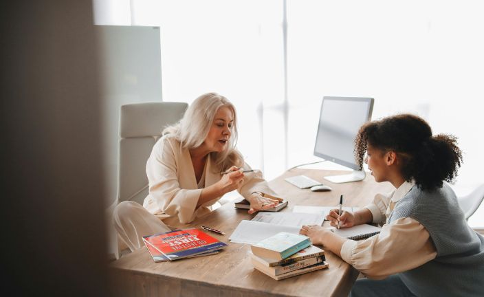 A guidance counselor speaking with a student at desk.