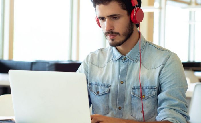 Young man wearing red headphones using laptop computer in community space.
