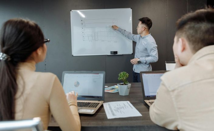 Two people with laptops watching man present on whiteboard.