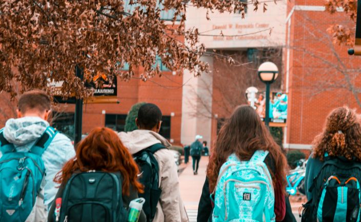 group of high schoolers wearing backpacks walking towards school entrance.