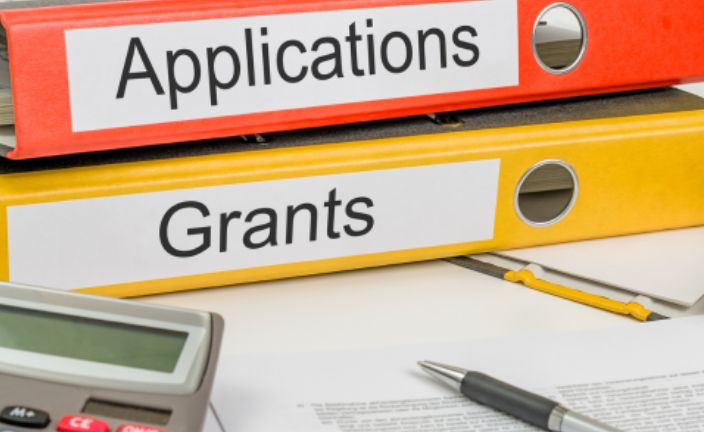 Orange and yellow binders on table that say applications and grants.