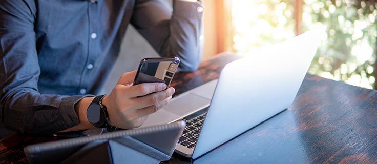 Man holding a phone while using his laptop.