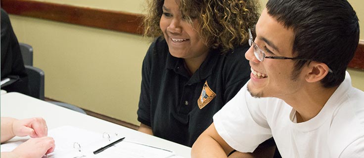 A man and woman smiling while learning within a classroom.