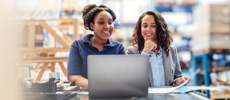 Two workers using a laptop within a warehouse.