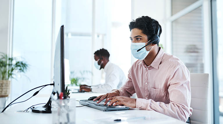 man sitting at a computer with a mask on.