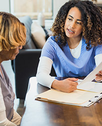 woman in scrubs talking to an older woman at a table.