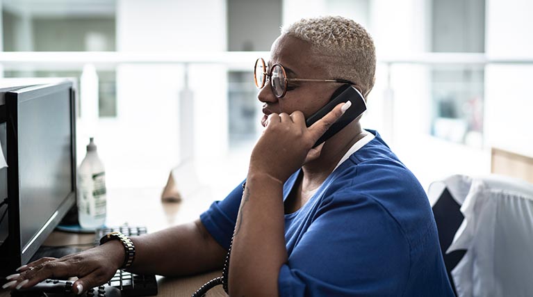 woman in scrubs on the phone sitting at a desk.