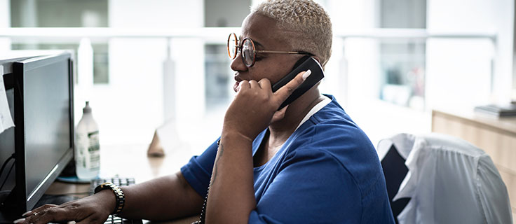 woman in scrubs on the phone sitting at a desk.