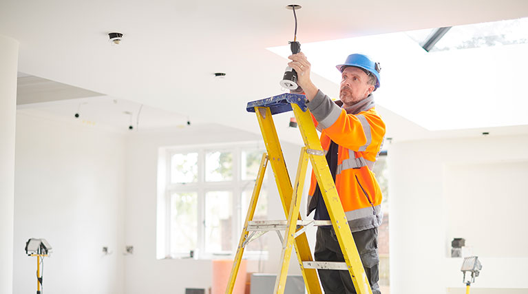 electrician on ladder installing lights in home